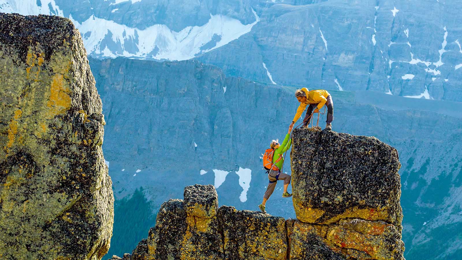 mountaineers scale rocks steps on cliff with rope